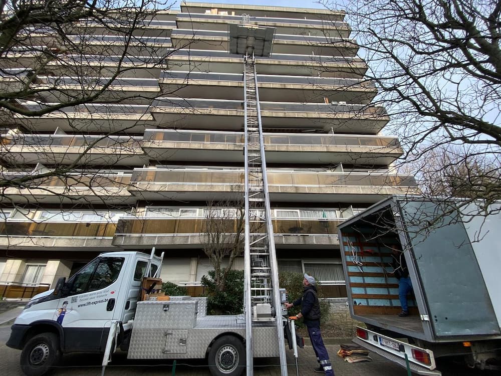 Vide maison Belgique en cours avec monte-charge et camions devant un immeuble à vider.